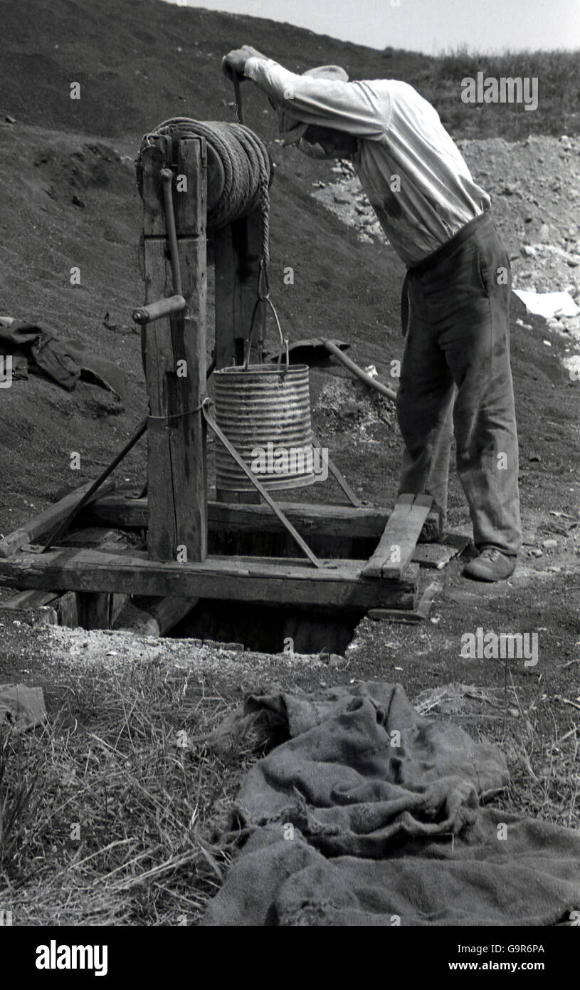 1930er Jahre, historisch, Mann drehen von hand zu Grundwasser bei einer selbstgemachten Stein strukturiert Brunnen oder Loch, Sudetenland, Tschechoslowakei. Stockfoto
