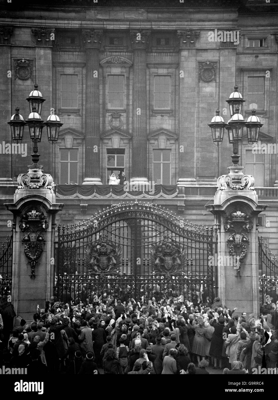 Die Braut und der Bräutigam winken vom Balkon, während sich Massen vor den Toren des Buckingham Palace versammeln, um das glückliche Paar zu begrüßen Stockfoto