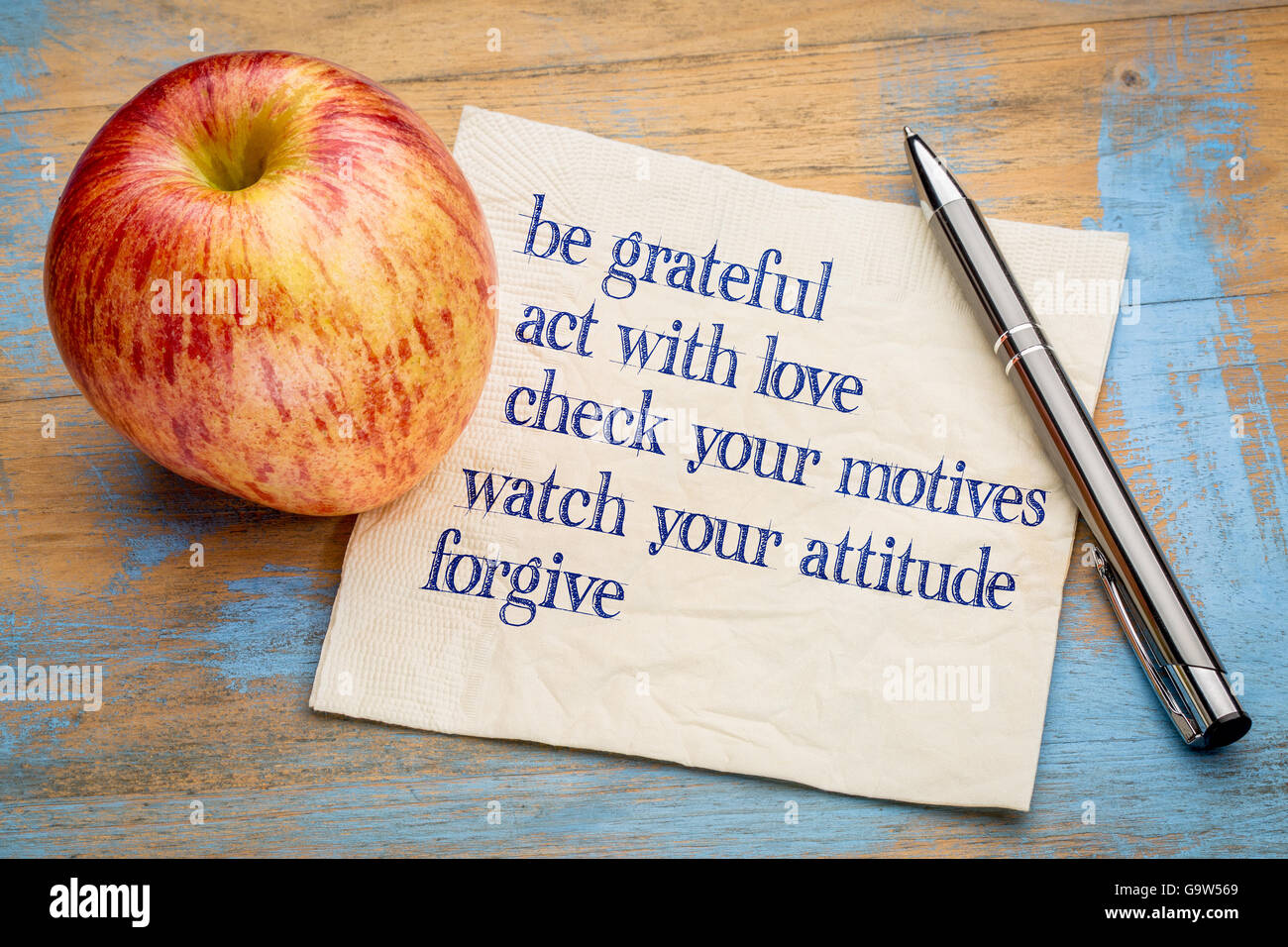 werden Sie dankbar und andere inspirierende Phrasen - Handschrift auf einer Serviette mit einem frischen Apfel Stockfoto