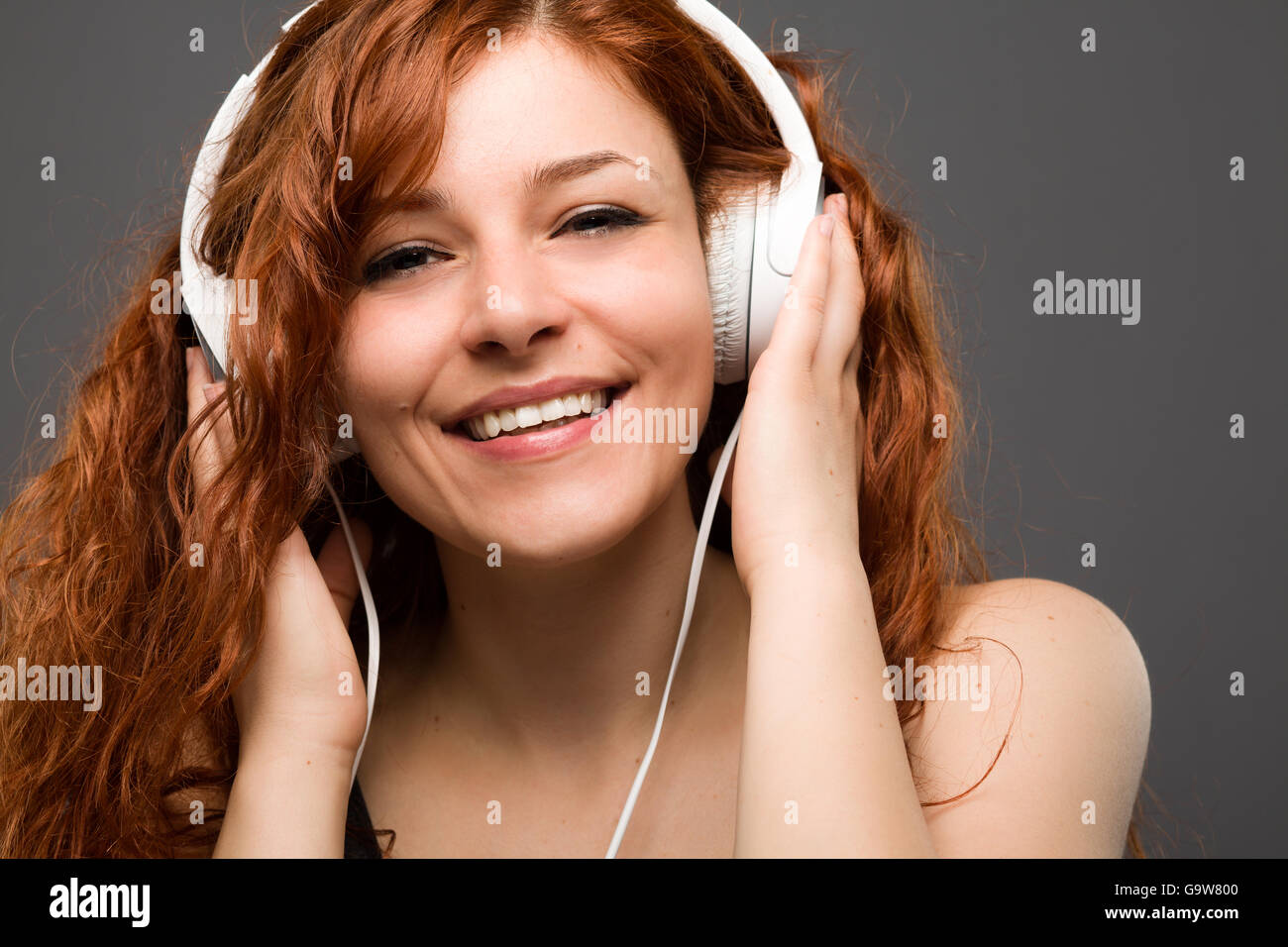 Lächelnde rothaarige Frau Musikhören mit Kopfhörer Stockfoto