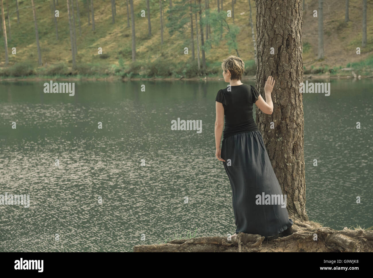 einsame junge Frau im langen Rock stehen am Ufer des Sees und Blicke in Ferne Stockfoto