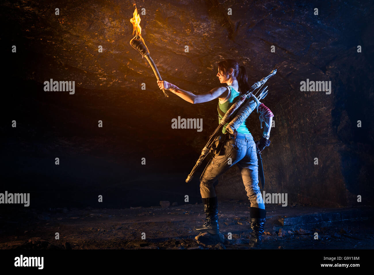Tomb Raider. Lara Croft-Charakter mit Fackel in der Hand, Messer in der anderen Höhlen erkunden. Trägt Pfeil und Bogen. Stockfoto