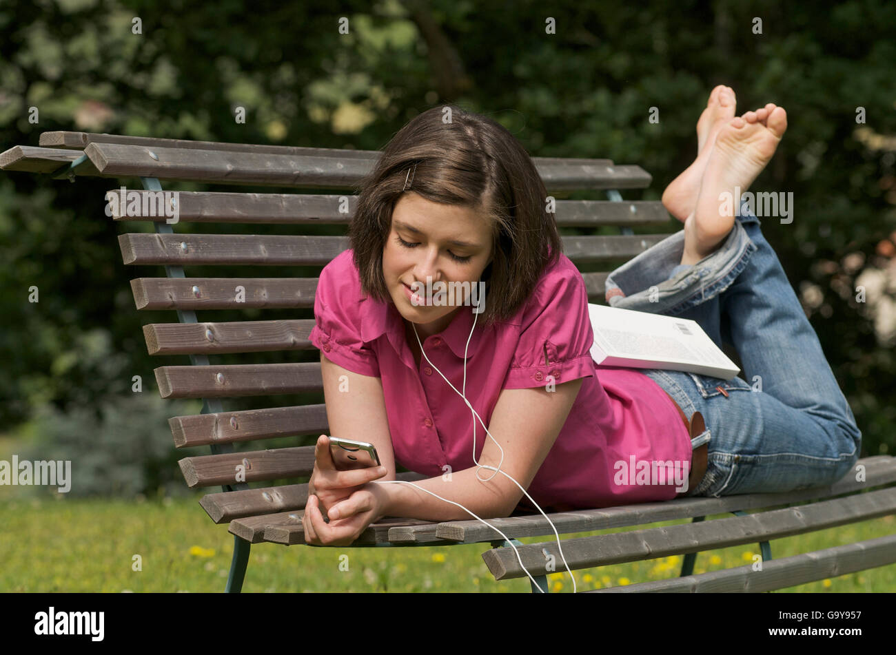 Junge Frau, liegend auf einer Bank in einem Park, Musik hören Stockfoto