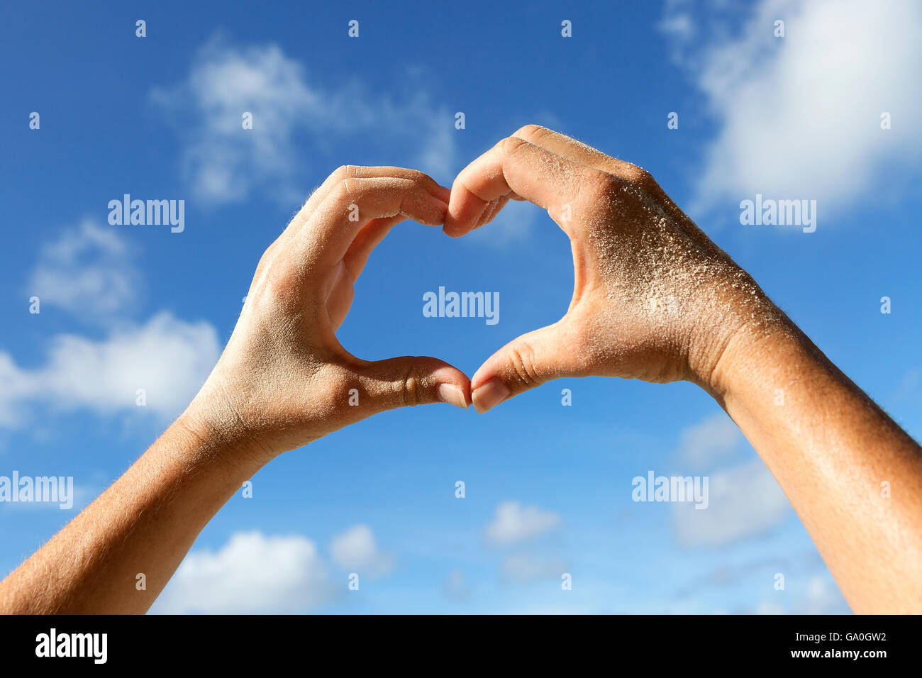 Weibliche Hände mit Sand zeigen Liebe Symbol mit blauem Himmel Stockfoto