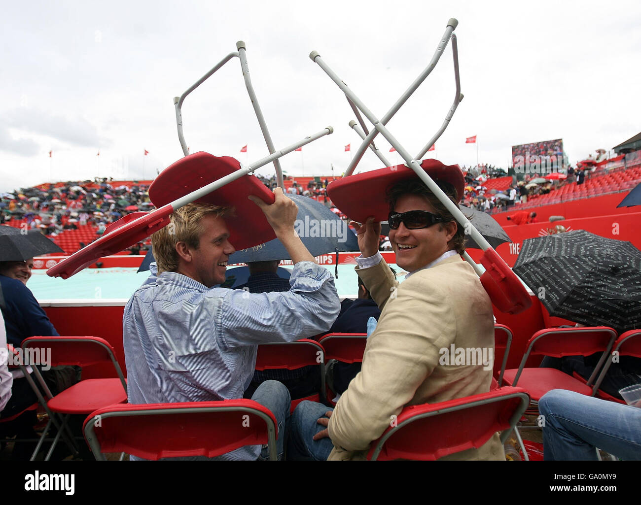 Fans nutzen Stühle, um sich während der Artois Championships im Queen's Club, London, vor dem Regen zu schützen. Stockfoto