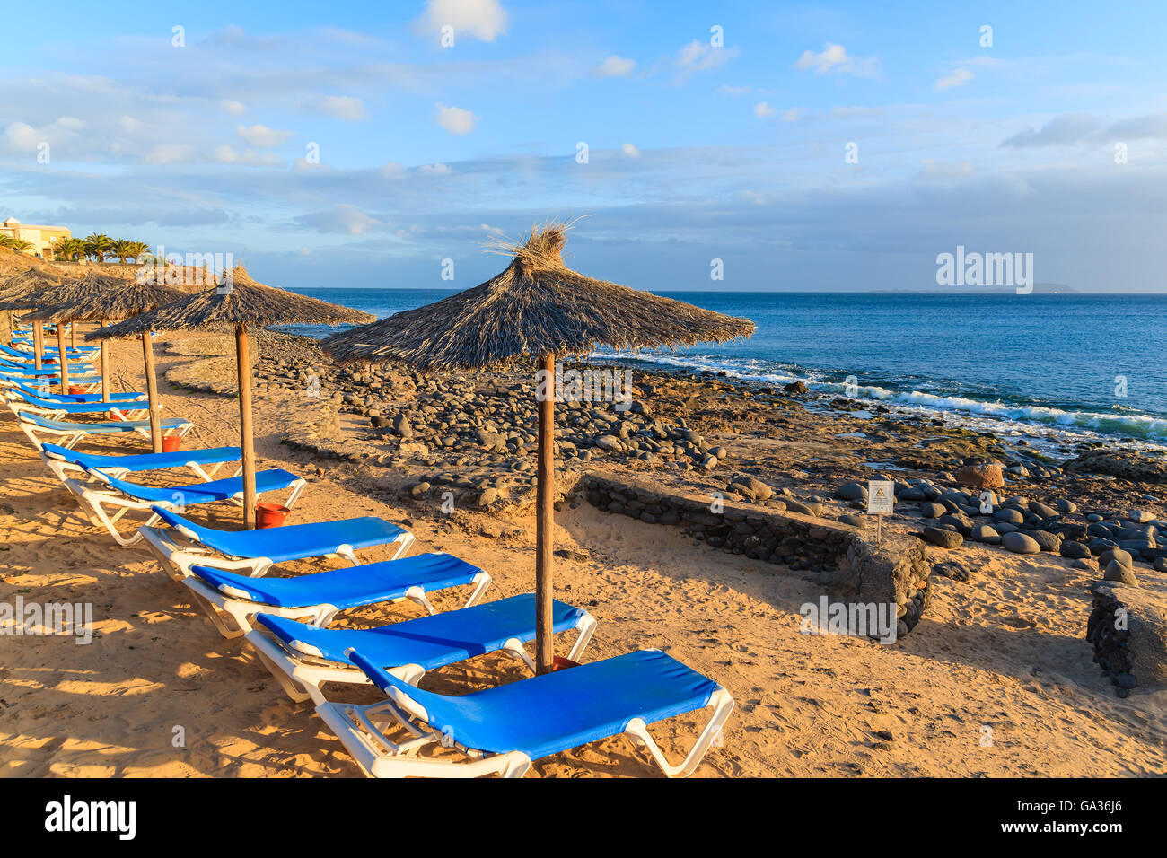 Reihe von Liegestühlen und Sonnenschirmen am Strand von Playa Blanca bei Sonnenuntergang, Lanzarote, Kanarische Inseln, Spanien Stockfoto