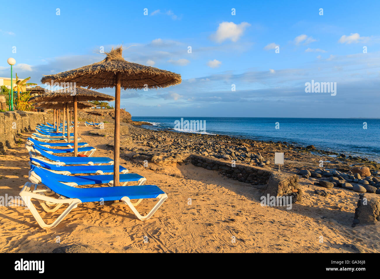 Reihe von Liegestühlen und Sonnenschirmen am Strand von Playa Blanca bei Sonnenuntergang, Lanzarote, Kanarische Inseln, Spanien Stockfoto