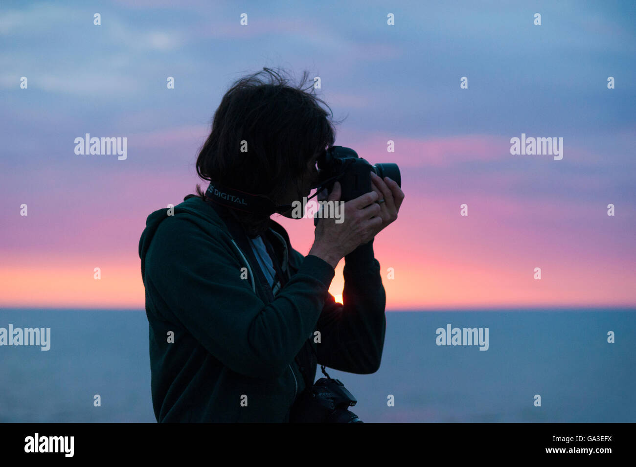 Eine Silhouette eines professionellen Fotografen Mannes mit dem Fotografieren mit einer DSLR-Kamera gegen einen Sonnenuntergang Stockfoto