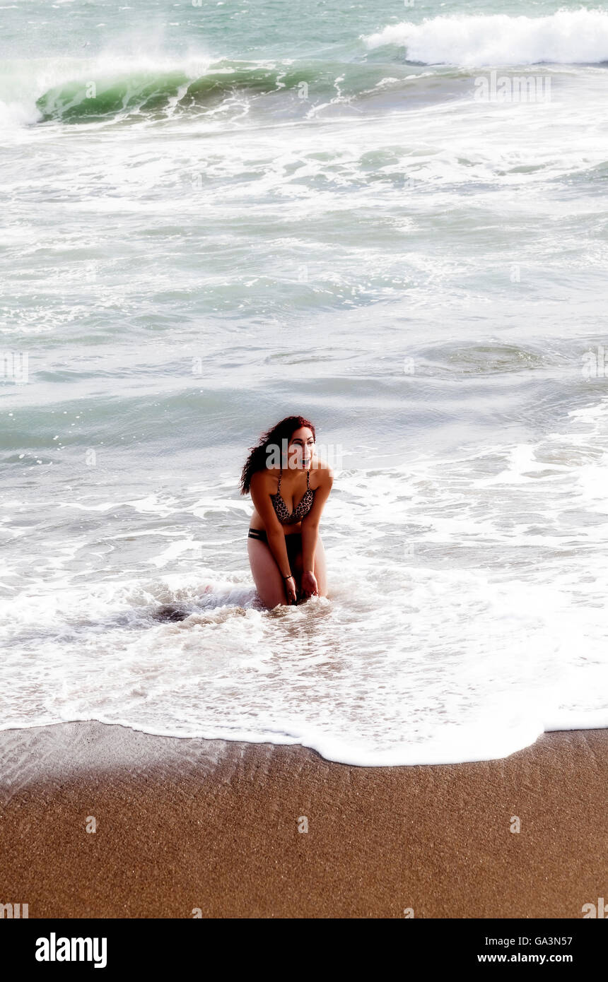 Latina Frau kniend In Meeresbrandung am Sandstrand Stockfoto