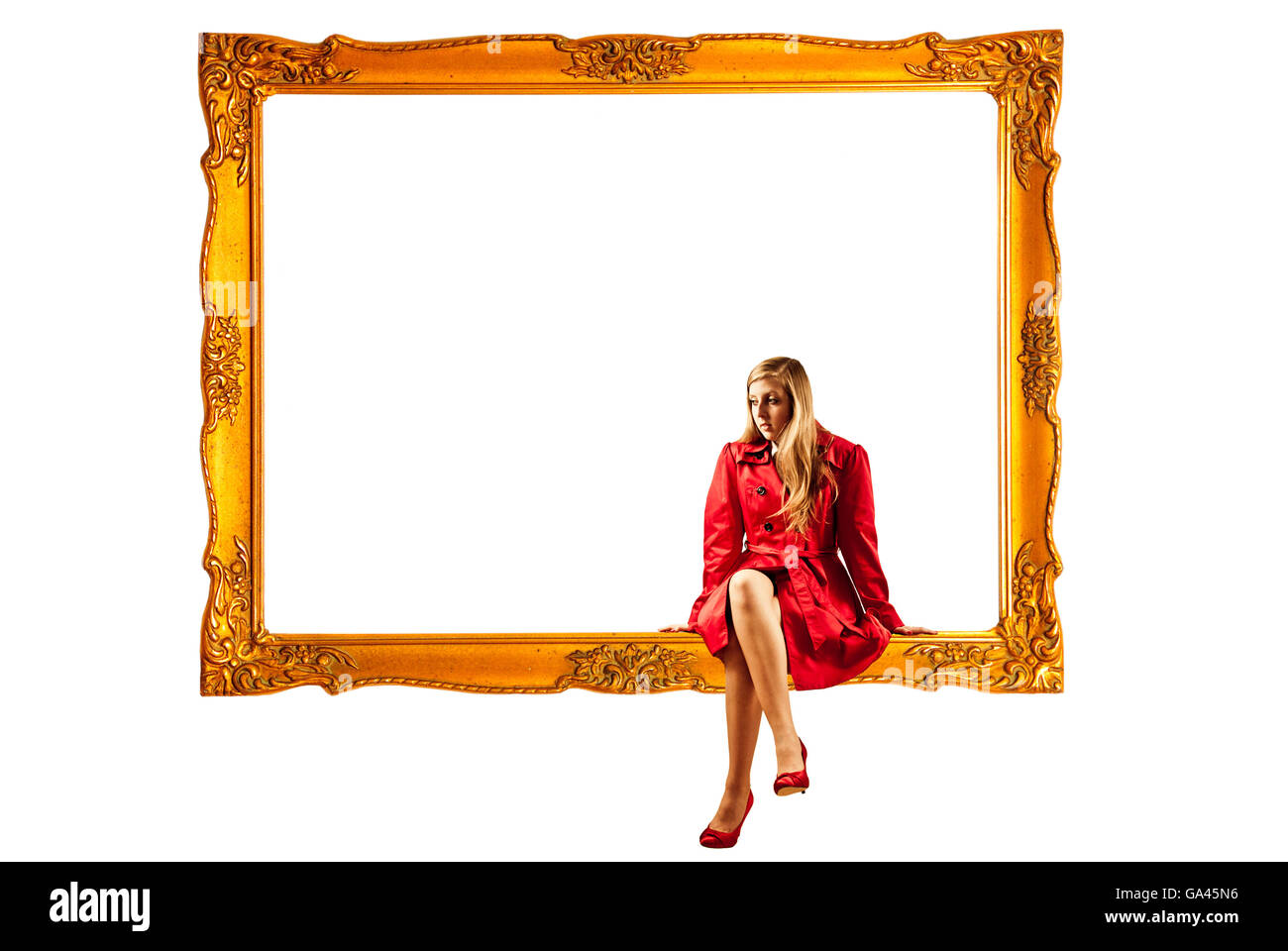 Blondes Mädchen im roten Mantel sitzt auf einem Bilderrahmen Stockfoto