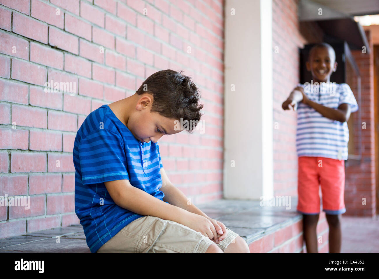 Schuljunge lachend auf traurige Klassenkamerad im Korridor Stockfoto