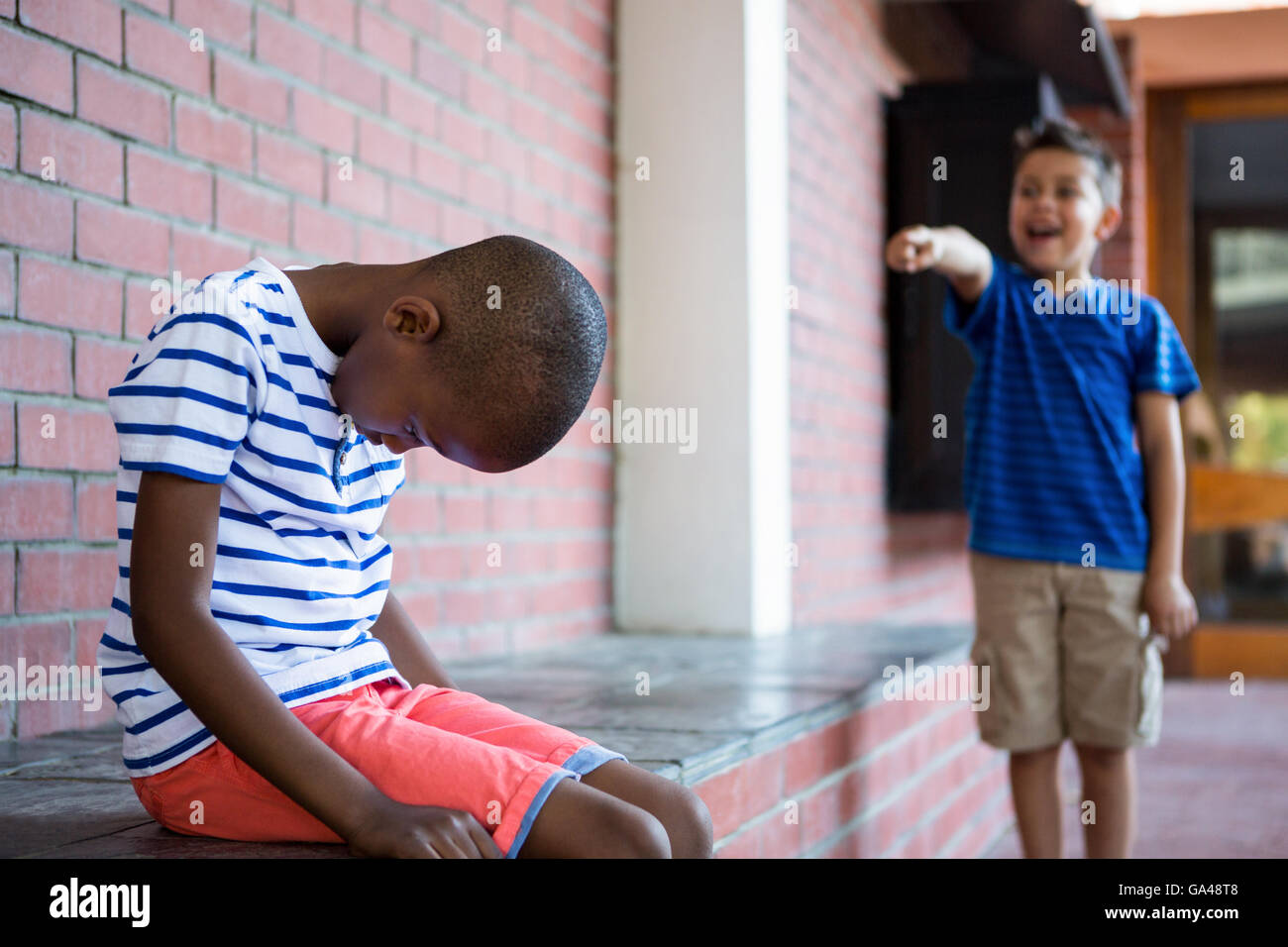 Junge lachend auf traurige Klassenkamerad im Korridor Stockfoto