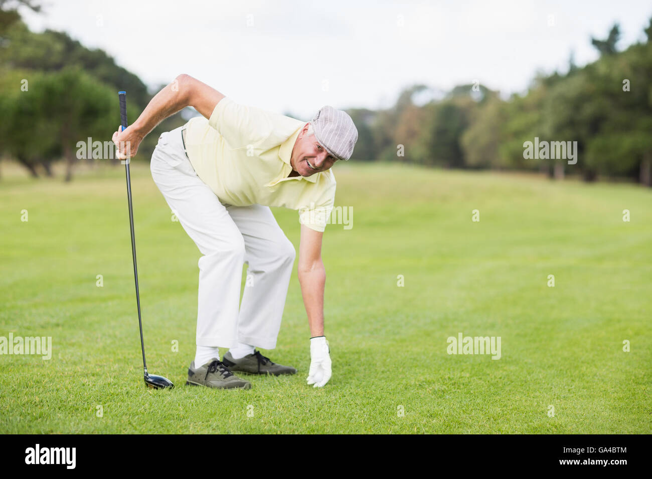 Reiferen Mann, der Golfclub beim Biegen auf Wiese hält lächelnd Stockfoto