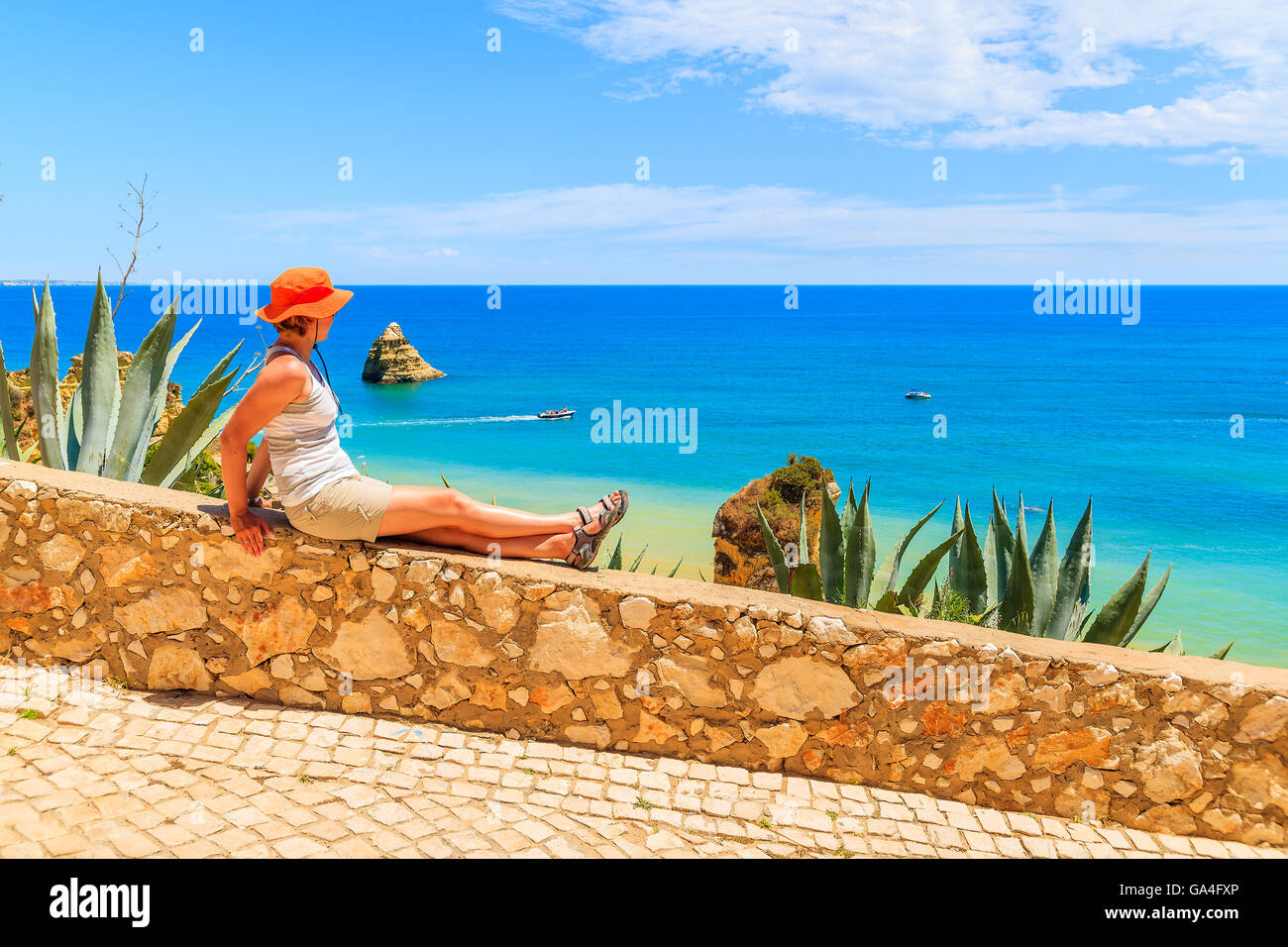 Junge Frau Tourist auf steinernen Brüstung sitzend und mit Blick auf Meer in der Nähe von Dona Ana Strand, Portugal Stockfoto