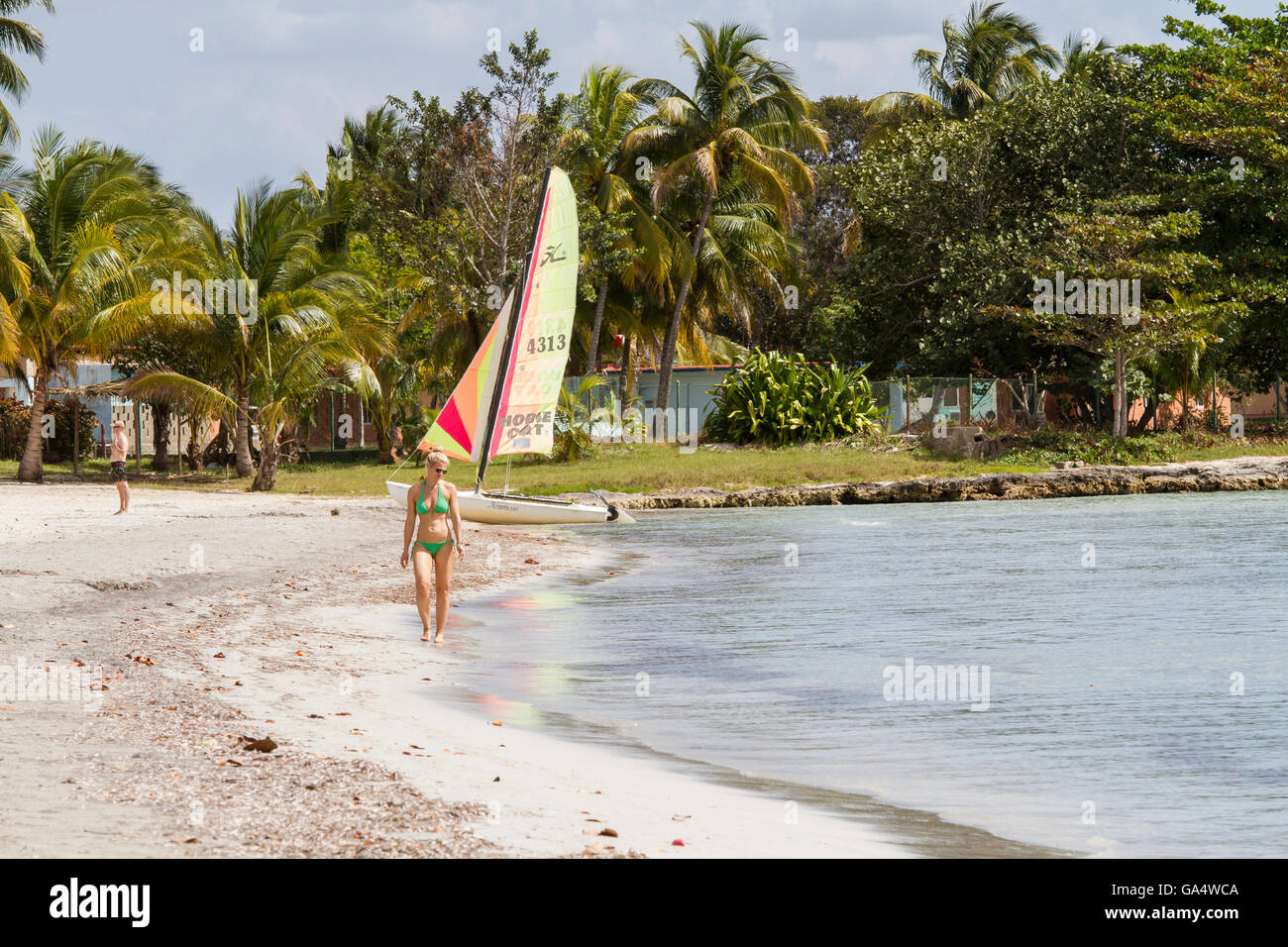 Frau im Bikini zu Fuß am Strand, mit Hobie Cat und Mann im Hintergrund, am Playa Larga, Kuba Stockfoto