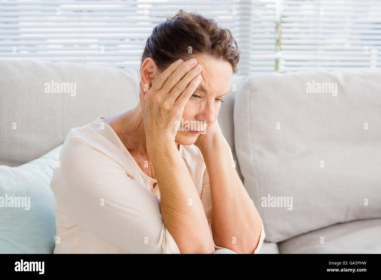 Frau mit Kopf in Händen sitzend auf sofa Stockfoto