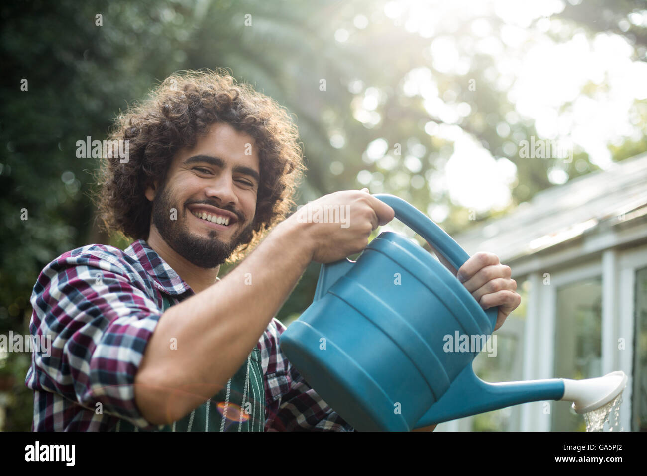 Glücklich Gärtner Bewässerung außerhalb Gewächshaus Stockfoto