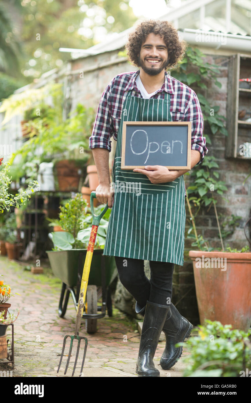 Männliche Gärtner mit Schild "geöffnet" Gartenarbeit Gabel halten Stockfoto