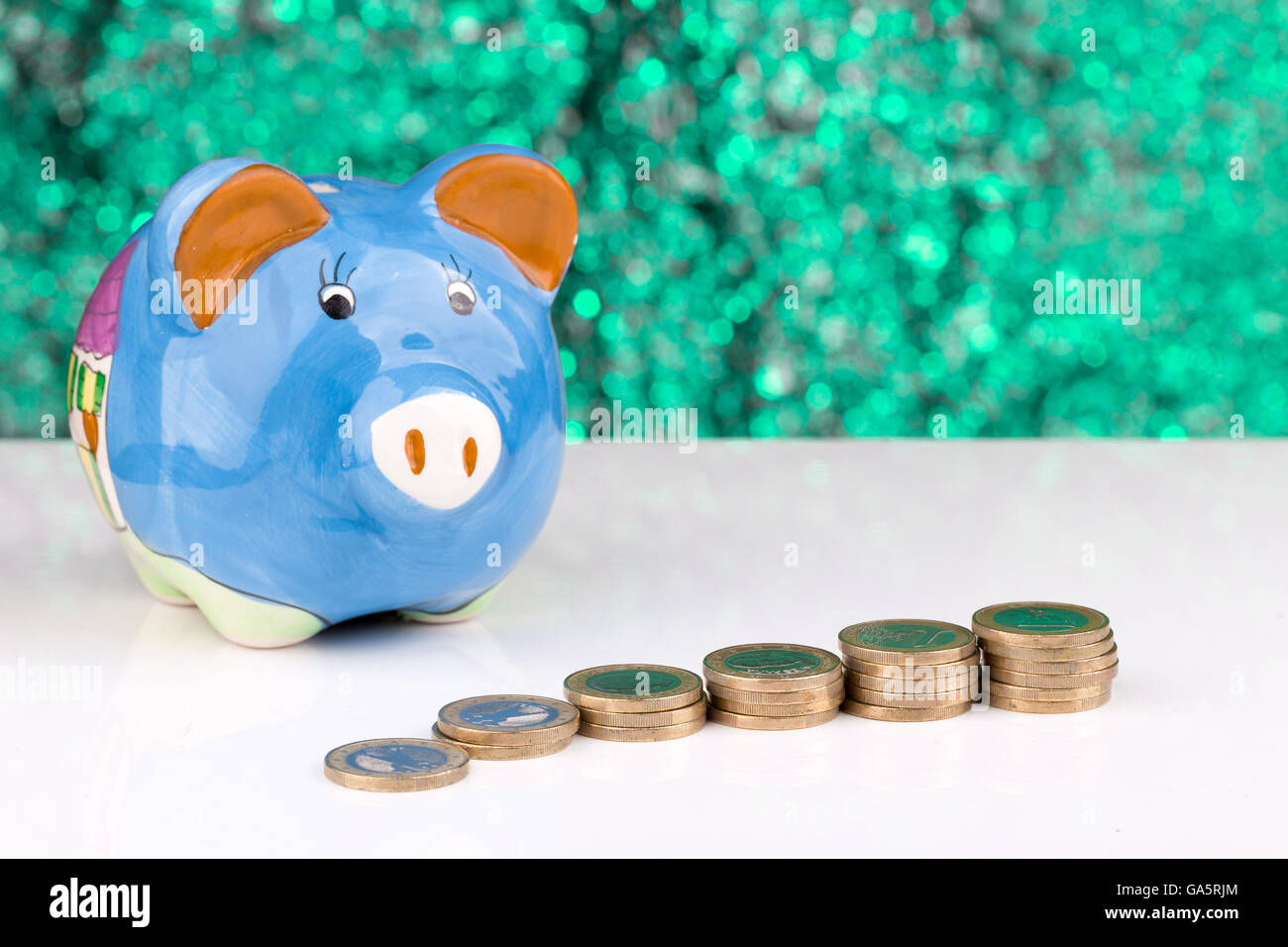 Blaues Sparschwein mit einem Stapel von Münzen und einem grünen Hintergrund Stockfoto