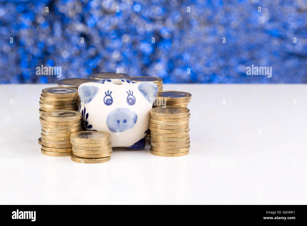 Sparschwein mit einem Stapel von Münzen und einem blauen verschwommenen Hintergrund Stockfoto