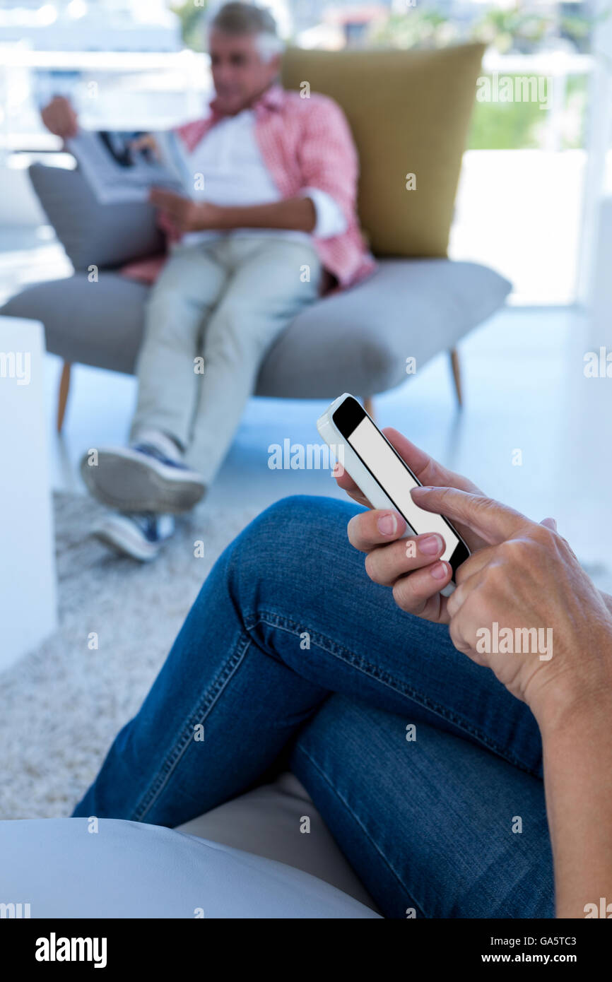 Mittelteil der Frau mit Telefon während Mann liest Zeitung Stockfoto