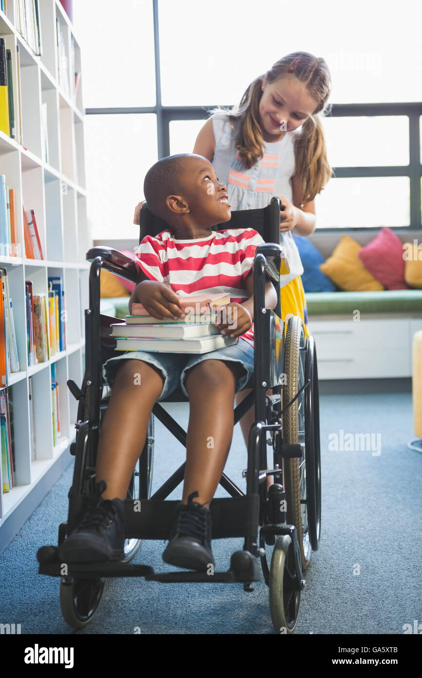 Glücklich Schulmädchen tragen Schüler im Rollstuhl Stockfoto