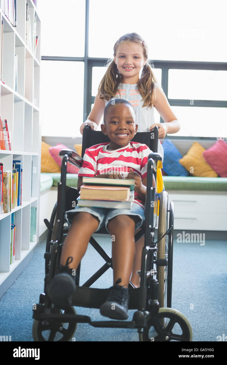 Glücklich Schulmädchen tragen Schüler im Rollstuhl Stockfoto