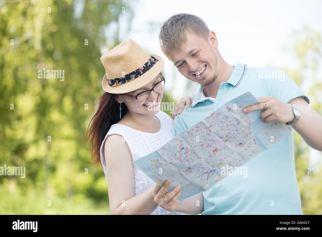 Fröhliche junges Reisen schöne Paar auf Sommertag Karte betrachten und lächelnd in der Straße stehen. Hübsche Frau, die trägt Stockfoto