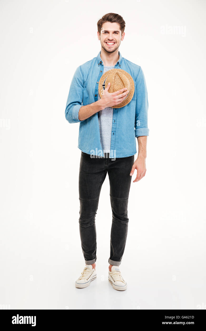 Fröhliche hübscher junger Mann stehen und halten Hut auf weißem Hintergrund Stockfoto