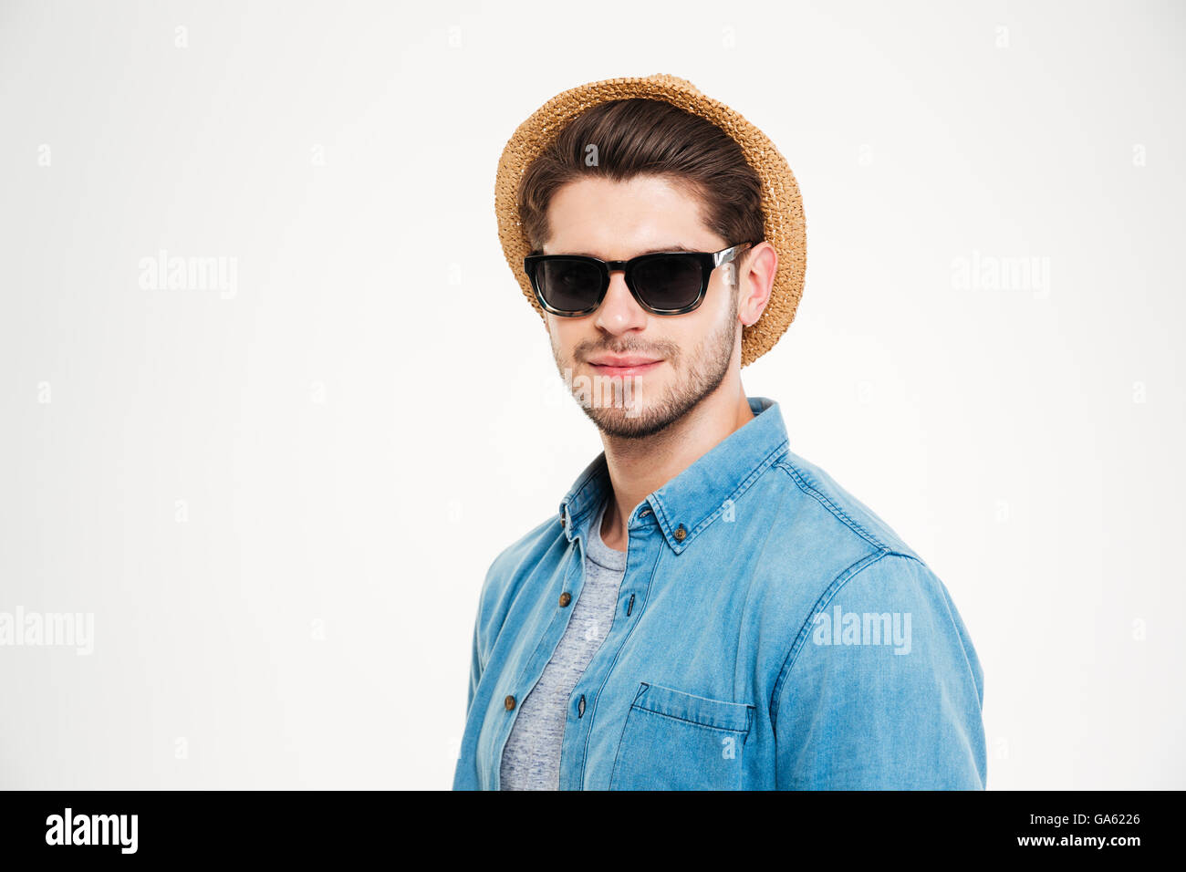Nahaufnahme von zuversichtlich junger Mann mit Sonnenbrille und Hut auf weißem Hintergrund Stockfoto