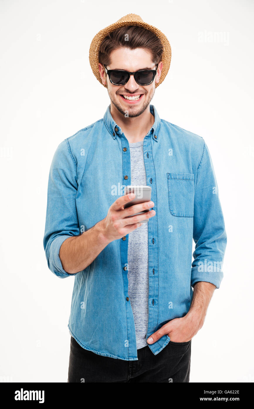 Fröhlichen jungen Mann in Hut und eine Sonnenbrille mit Smartphone auf weißem Hintergrund Stockfoto