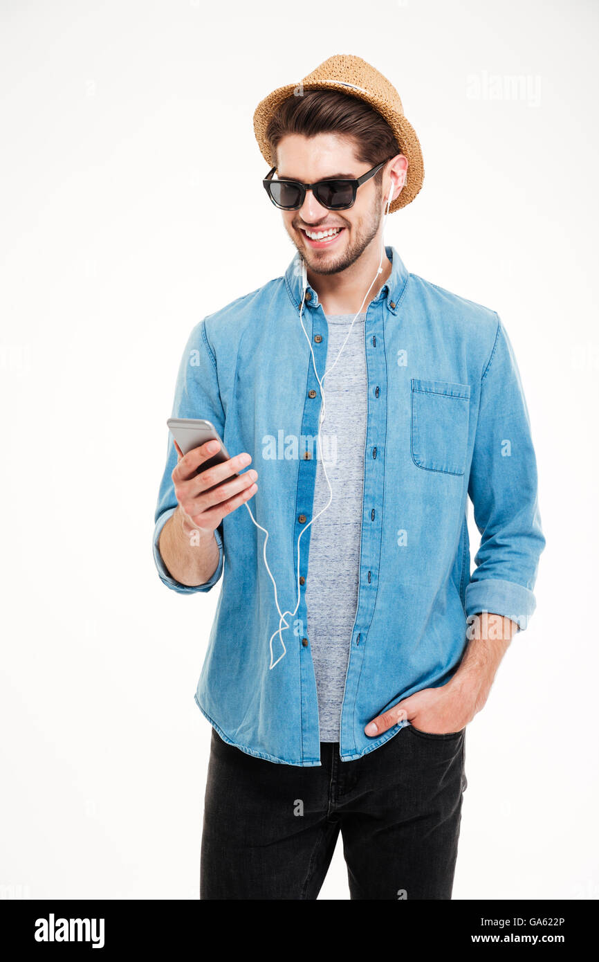 Fröhliche junger Mann mit Sonnenbrille und Hut stehend und mit smartphone Stockfoto