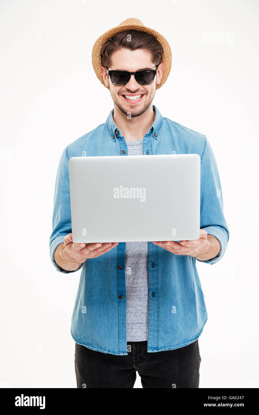 Fröhliche attraktiver junger Mann mit Sonnenbrille und Hut mit laptop Stockfoto
