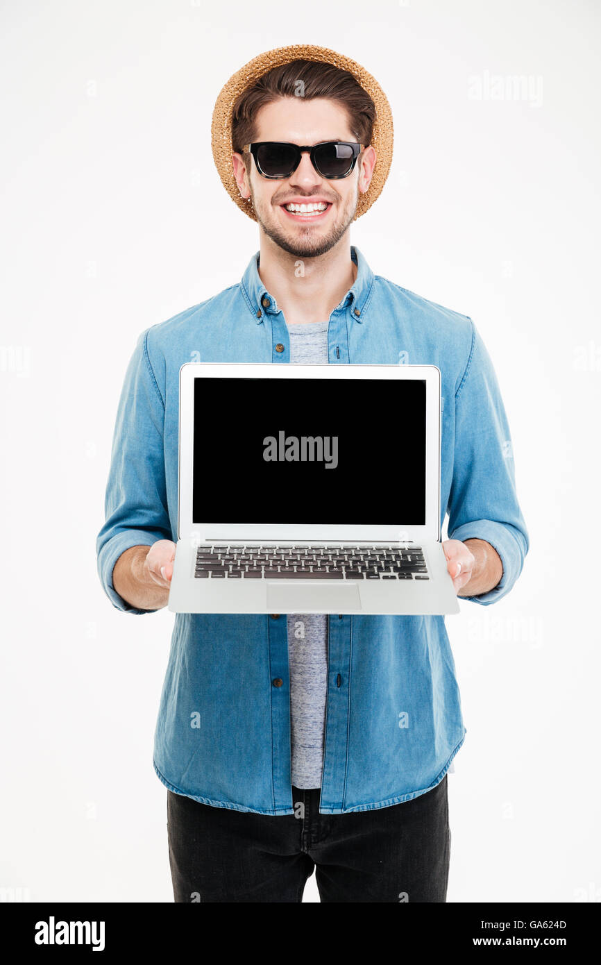 Jungen Mann mit Sonnenbrille und Hut stehen und leerer Bildschirm Laptop hält lächelnd Stockfoto