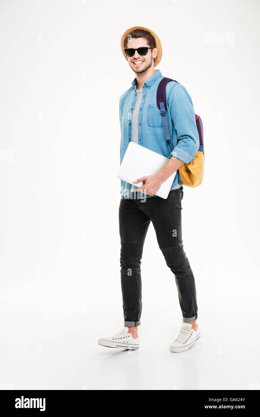 Voller Länge von fröhlichen jungen Mann mit Rucksack wandern und wenn Sie mit Laptop auf weißem Hintergrund Stockfoto