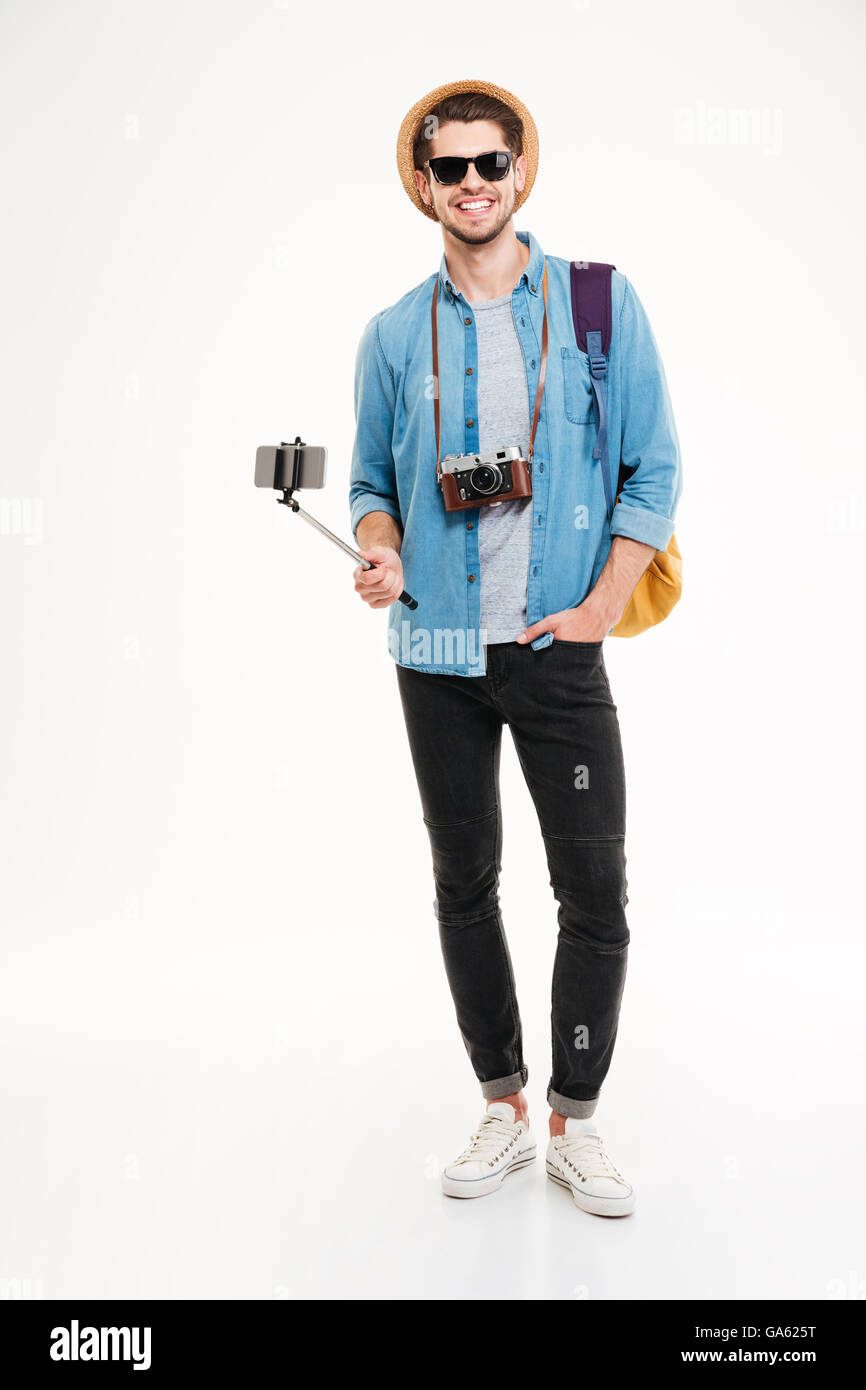 Glückliche junge Touristen mit Rucksack, Vintage-Kamera oder Smartphone auf Selfie Stick auf weißem Hintergrund Stockfoto
