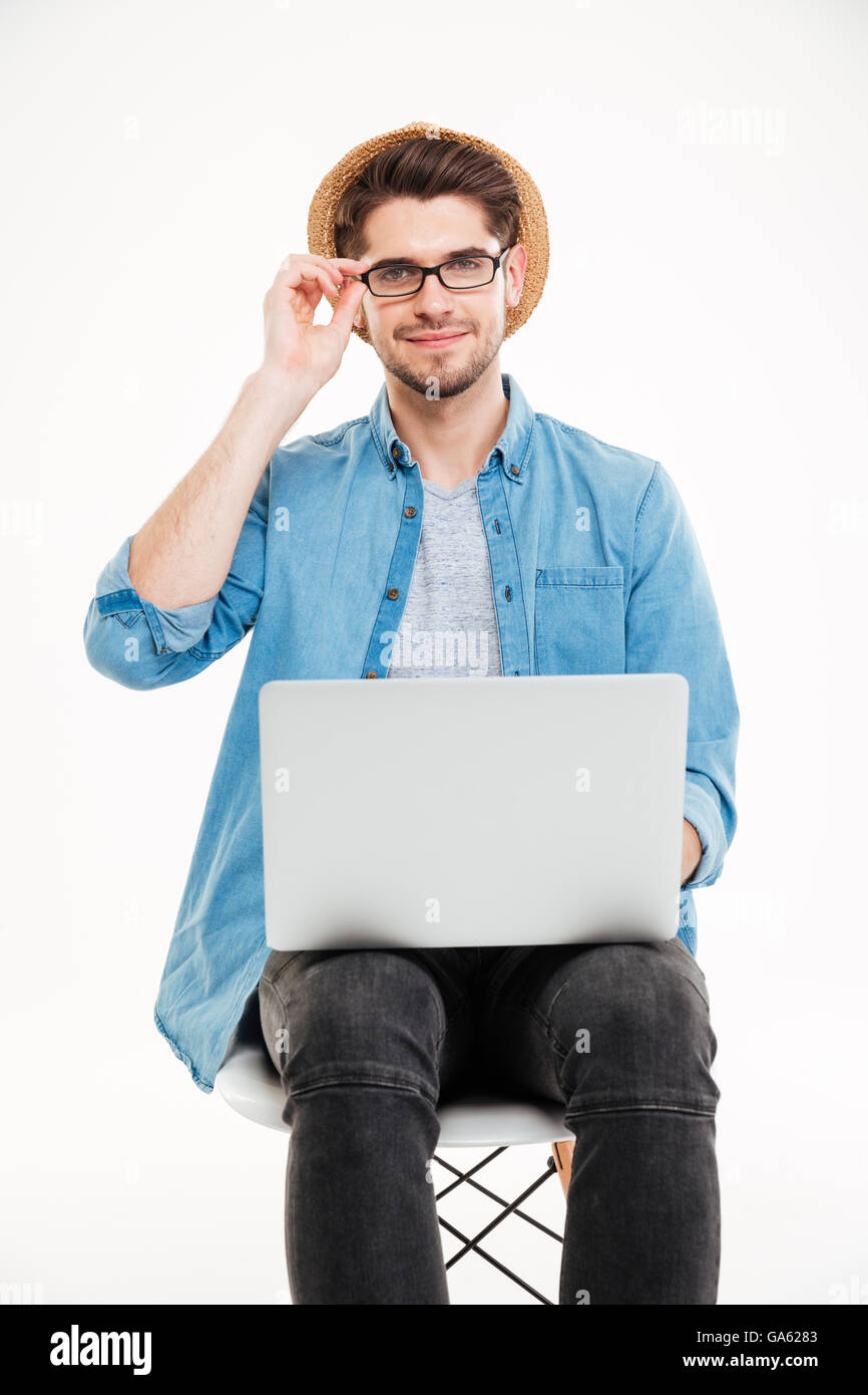 Lächelnden jungen Mann in Gläsern und Hut mit Laptop auf weißem Hintergrund Stockfoto