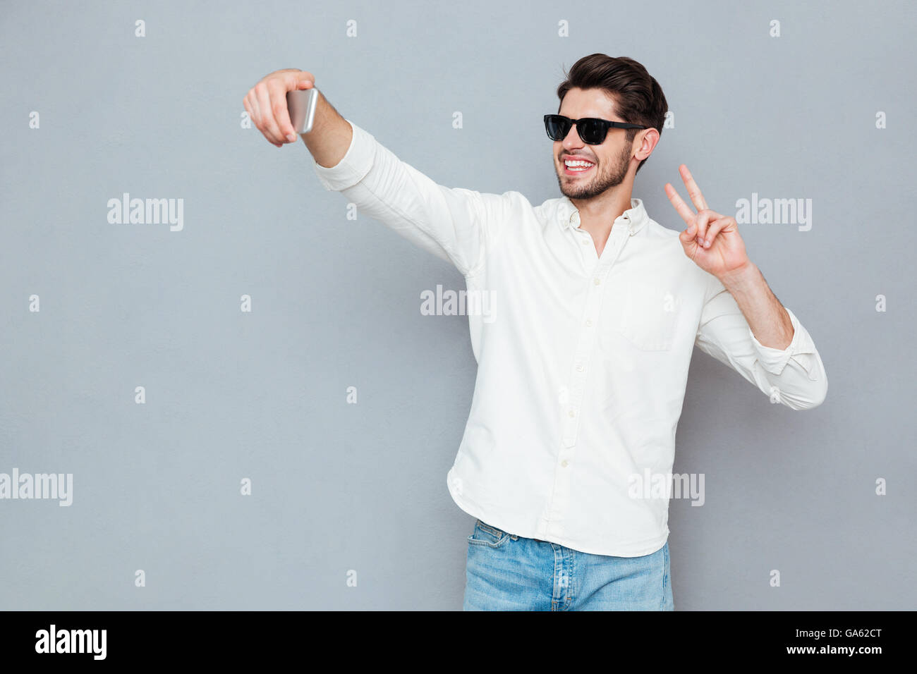 Glücklich Jüngling machen Selfie Foto auf Smartphone über grauen Hintergrund Stockfoto