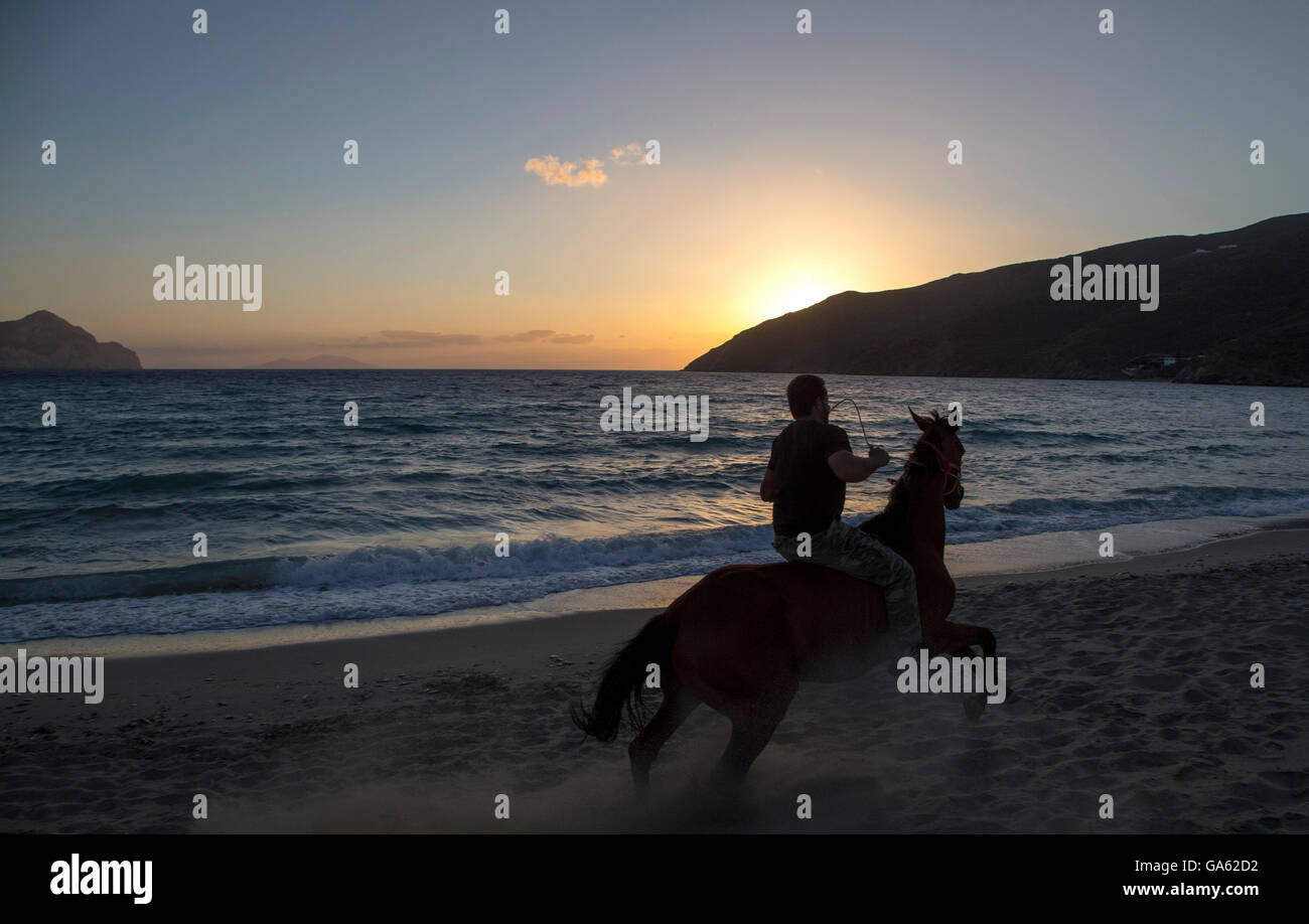 Ein Mann Reitpferd am Strand und atemberaubenden Sonnenuntergang in Amorgos Island, Griechenland Stockfoto