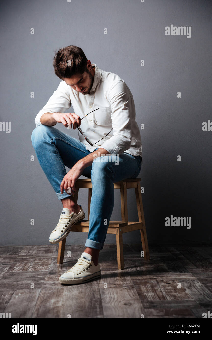 Traurig wütend junger Mann sitzen und blickte auf grauem Hintergrund Stockfoto