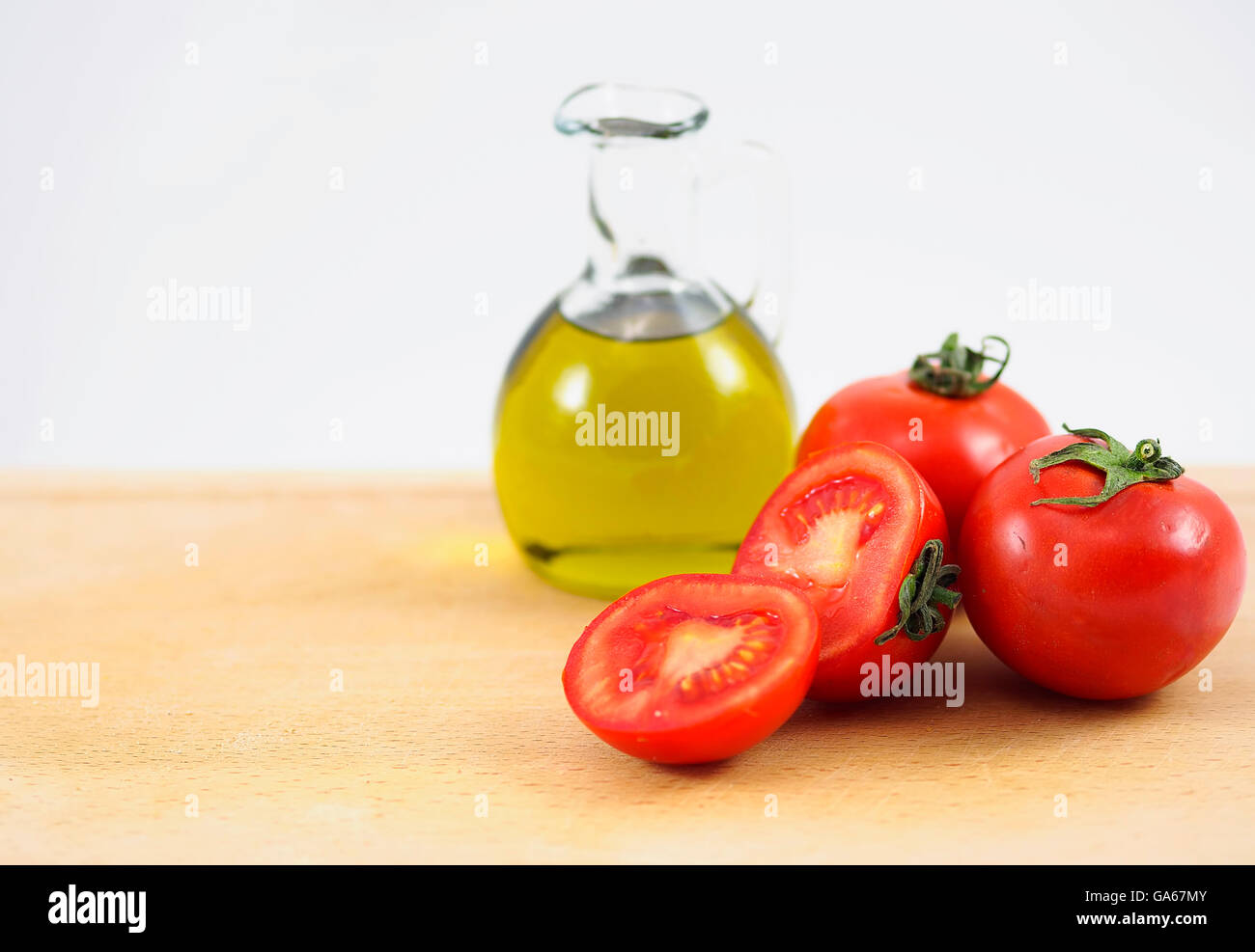 Öl-Kanne, voller Evo Öl und rote Tomaten auf einem Holztisch. Stockfoto
