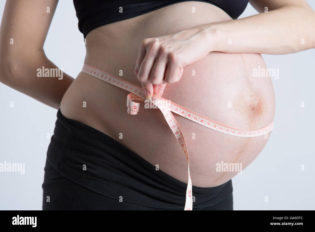 Eine schwangere Frau hält ein Maßband um ihre schwangeren Bauch. Stockfoto