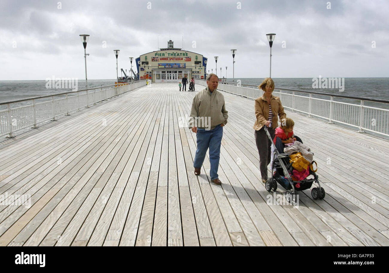 Eine Familie rast heute am Pier in Bournemouth in Dorset gegen den Wind, wo der goldene Sand aufgrund des schlechten Augustwetters fast vollständig verlassen war. Stockfoto