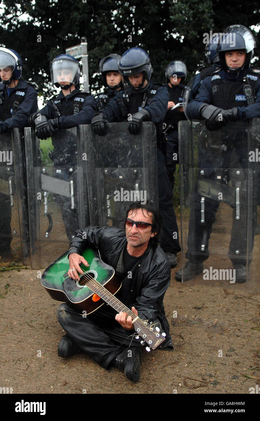 Ein Protestler im Klimacamp in Sipson nahe dem Flughafen Heathrow sitzt vor der Bereitschaftspolizei und spielt seine Gitarre. Stockfoto