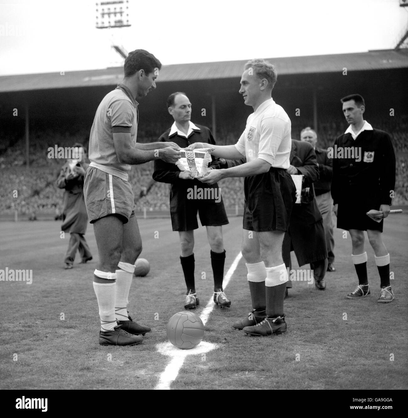 Brasilianischer Kapitän Nilton Santos (l) und sein England-Amtskollege Billy Wright (r) tauschen Wimpel aus, während Schiedsrichter Maurice Guigue anschaut. Stockfoto