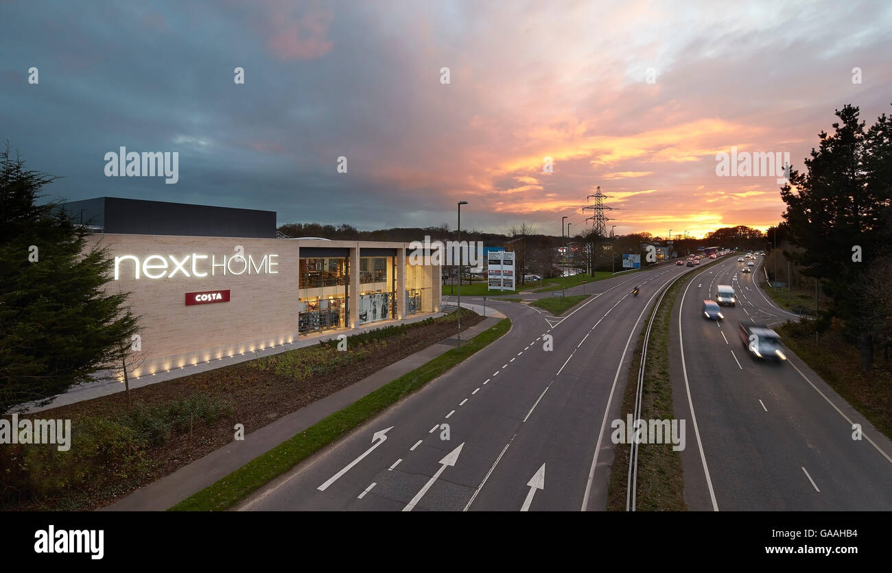 Kontextbezogene Ansicht mit Straße bei Sonnenuntergang. Next - Haus und Garten Shops, Southampton, Vereinigtes Königreich. Architekt: Stanton Williams, 2014. Stockfoto