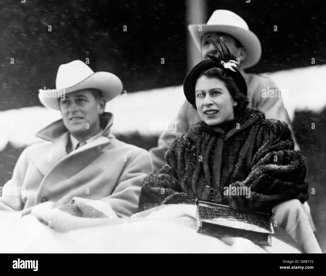 Bedeckt mit Decken und genießen sich trotz eines Schneesturms Prinzessin Elizabeth und der Herzog von Edinburgh beobachten ein "Stampede"-Rodeo, das speziell für sie in Calgary, Alberta, während ihrer Tour durch Kanada inszeniert wird. Calgarys erste Winteransturm beinhaltete das Reiten von Cowboys auf ungebrochenen Pferden und wilden Steern. Stockfoto