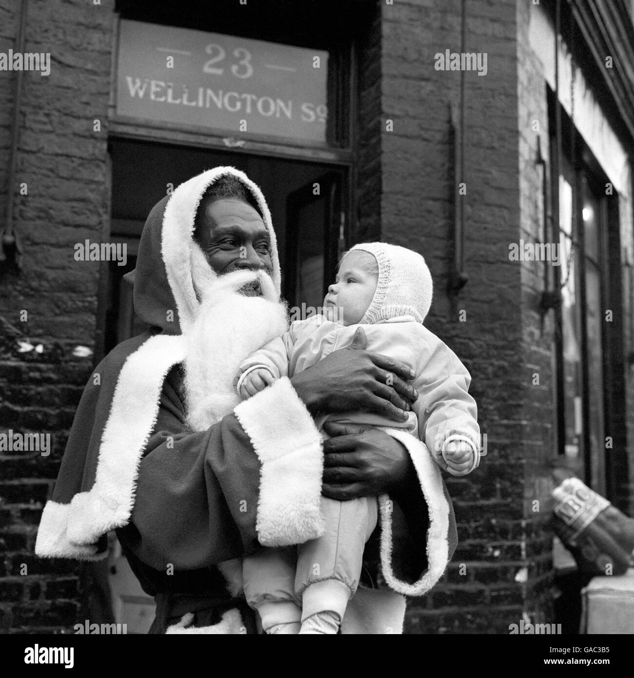 Joe Cole, der vor zwanzig Jahren aus Nigeria nach Großbritannien kam, ist Weihnachtsmann in Philip Townsends Laden in der Little Clarendon Street, Oxford. Santa Joe, gesehen mit dem neun Monate alten Jeremy Taylor, bekam den Job, weil er der glücklichste und fröhlichste Mensch war, den Herr Townsend finden konnte. Stockfoto