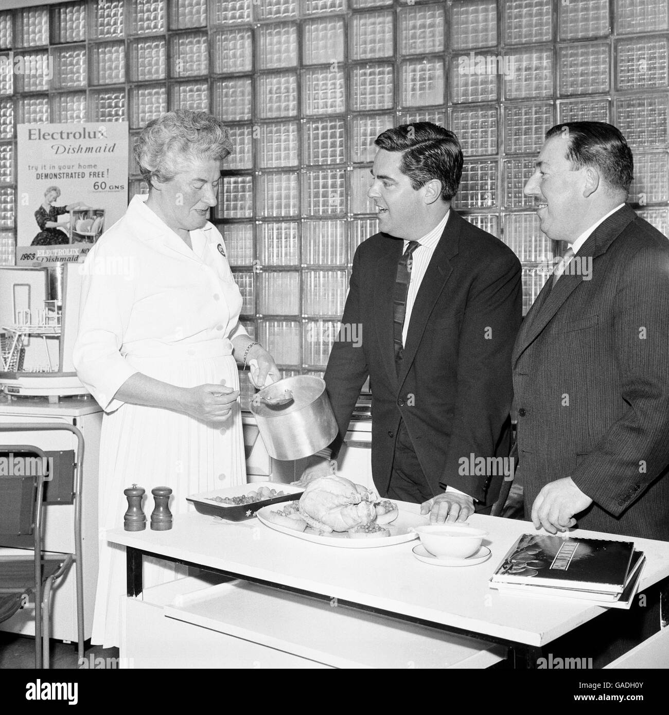 Herr Robert Carrier (Mitte) Gourmet- und Essensschriftsteller, sieht Miss Mary Barnard, eine leitende Demonstratorin am London Electricity Board, heute im Showroom des Boards in der Regent Street, London, eine Mahlzeit mit gekochtem Huhn, Gemüse und Saucen zubereiten. Stockfoto