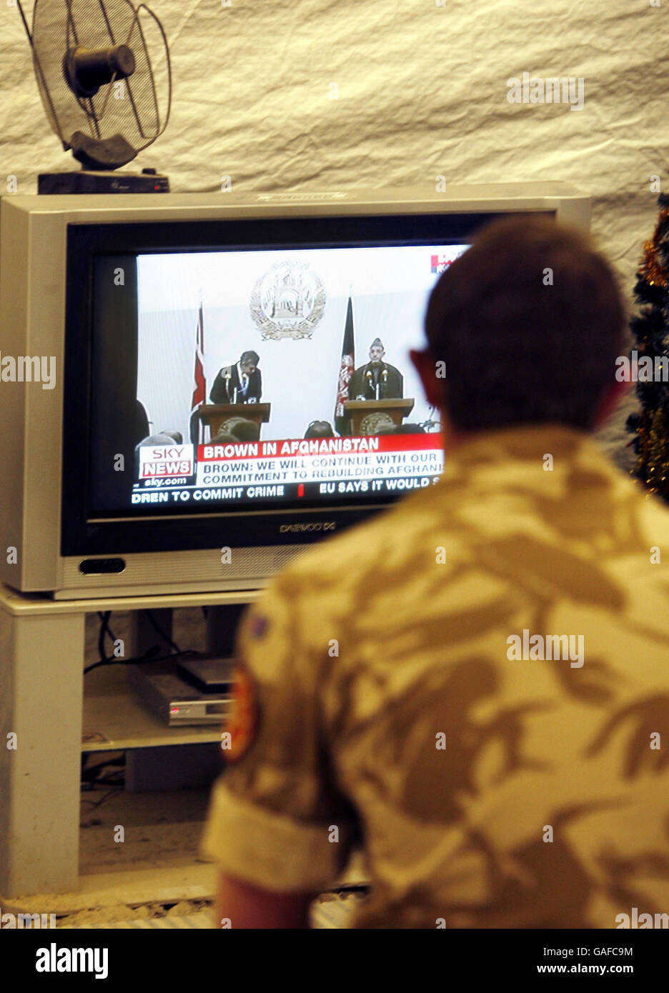 Ein Mitglied der britischen Streitkräfte beobachtet die Afghanistan-Ankündigung von Premierminister Gordon Brown auf einem Fernsehgerät im Camp Bastion in der Provinz Helmand in Afghanistan. Stockfoto